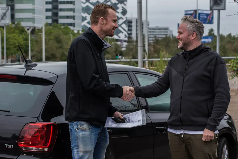 Een klant en een medewerker schudden elkaar de hand naast de auto bij de overdracht